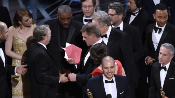 Fred Berger, producer of "La La Land," foreground center, gives his acceptance speech as members of PricewaterhouseCoopers, Brian Cullinan, holding red envelope, and Martha L. Ruiz, in red dress, and a stage manager discuss the best picture announcement error among the cast at the Oscars on Sunday, Feb. 26, 2017, at the Dolby Theatre in Los Angeles. The actual winner of best picture went to "Moonlight." (Photo by Chris Pizzello/Invision/AP)