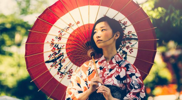 Beautiful japanese woman stand in the park. She wears kimono, obi and hold oil paper umbrella.The kimono is very colorful and elegant. She seems very pensive.